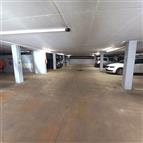 Podzemní garážové stání s betonovou podlahou, dostatečně osvětlené zářivkami, s několika zaparkovanými auty, nabízí bezpečné parkování.